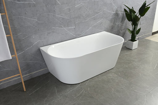 White freestanding bathtub in a modern bathroom with gray tiles and a plant.